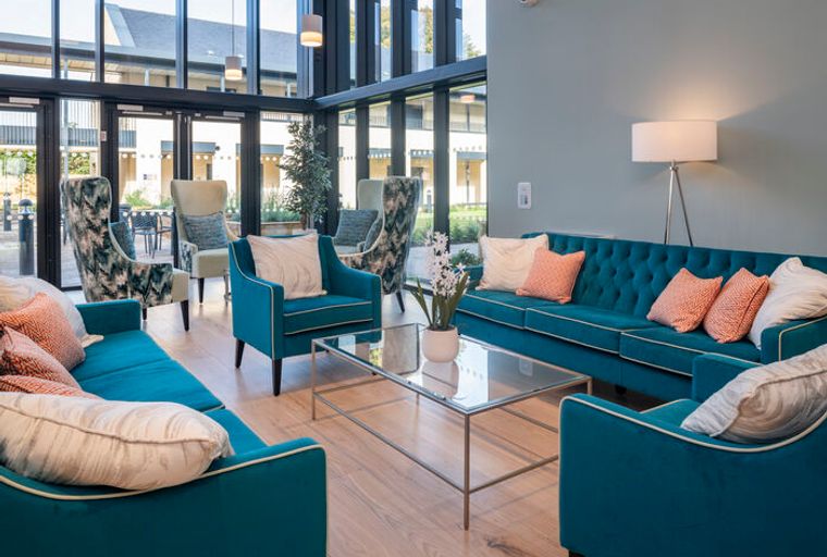 A living room with teal sofas, accent chairs, and a glass coffee table.