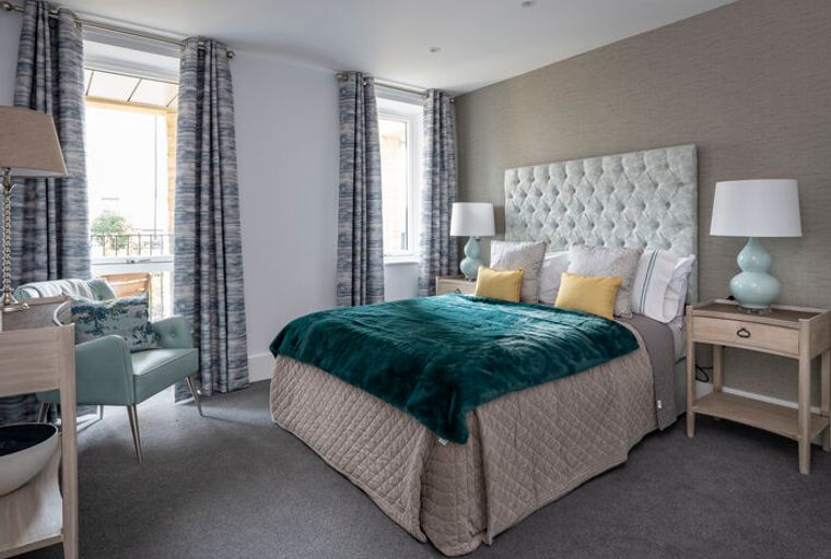 A bedroom with a bed, headboard, bedside tables, lamps, armchair, and curtains.