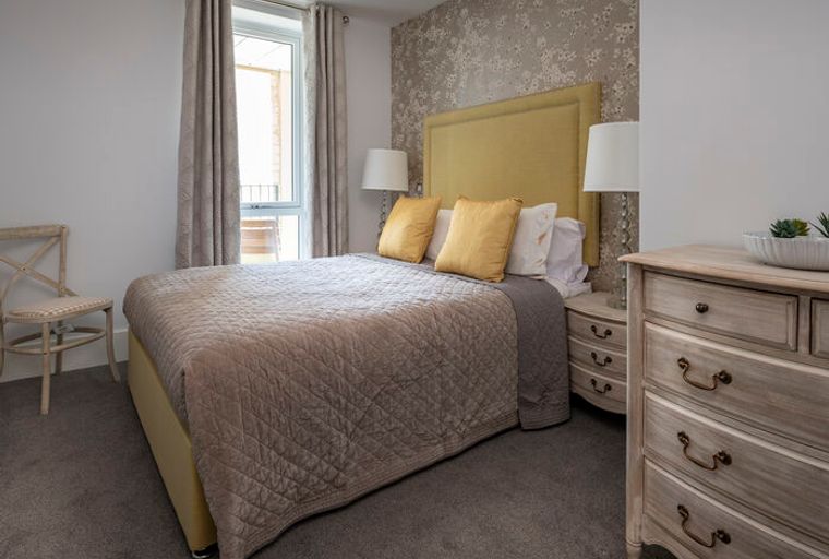 A bedroom with a bed, pillows, lamps, a chair, and a dresser.