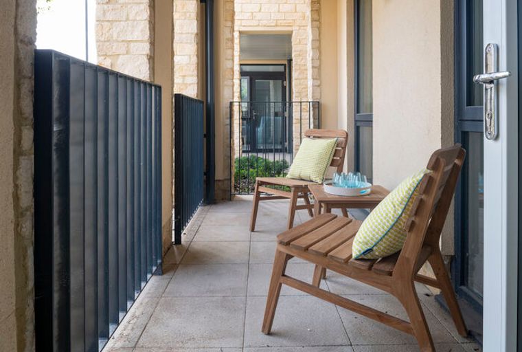 A balcony with two wooden chairs, a small table, and decorative pillows.