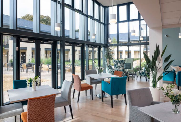 A communal dining area with tables and chairs next to large windows.