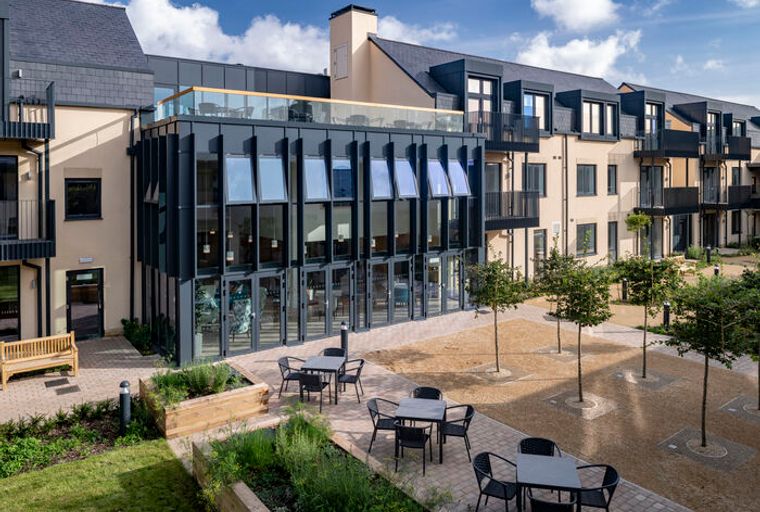 A modern building with a glass facade and balconies overlooking a courtyard with outdoor seating.