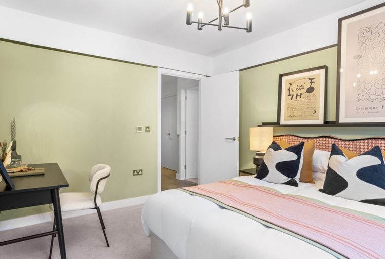 A bedroom with a bed, pillows, a desk, a chair, and artwork.