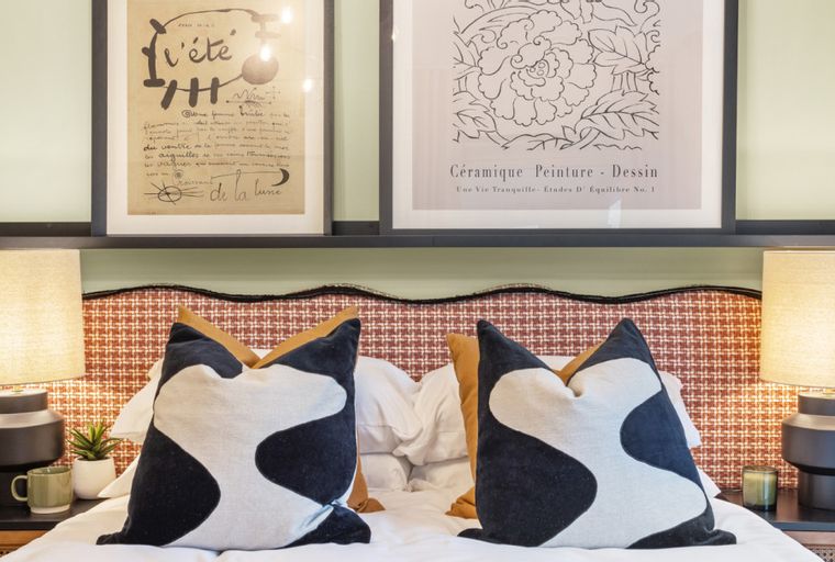 A bedroom with a bed, headboard, pillows, bedside lamps, and framed art.