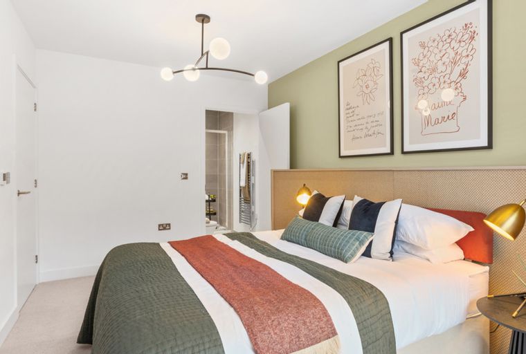 A bedroom with a bed, pillows, a throw, bedside lamps, framed art, and a chandelier.