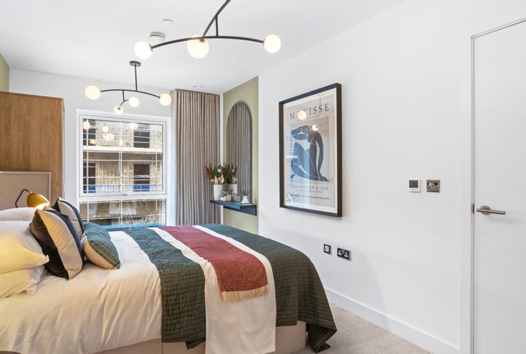 A bedroom with a bed, pillows, a comforter, a chandelier, a lamp, a window, and artwork.
