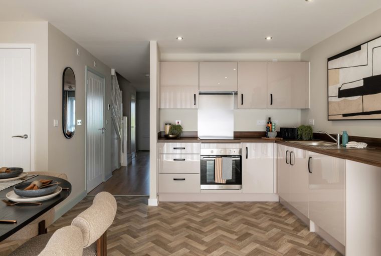 A modern kitchen and dining area with sleek cabinetry, a herringbone floor, and a dining table set for a meal.