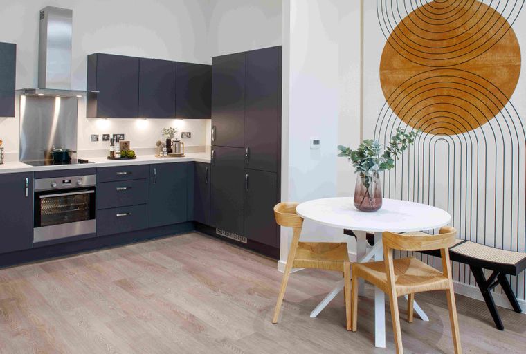 A kitchen and dining area with dark cabinets, a built-in oven, a round table, and chairs.