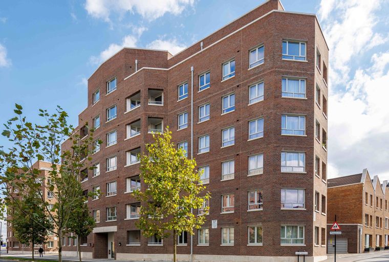 A modern brick apartment building with multiple windows and trees in front.