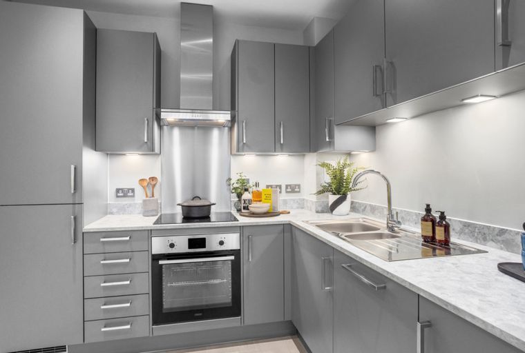 A modern grey L-shaped kitchen with integrated appliances, a double sink, and under-cabinet lighting.