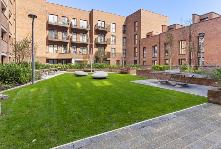 A courtyard with a lawn, ping pong table, and seating areas surrounded by brick buildings.