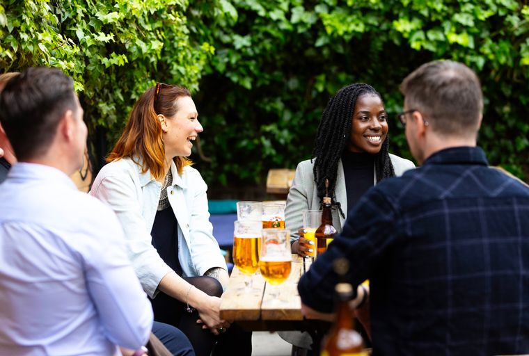 A group of people sitting at a wooden table outdoors with drinks.
