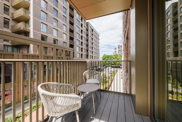 A balcony with two chairs and a table overlooking a street between buildings.