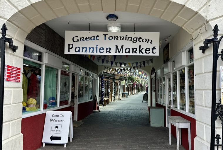 A view down a market arcade with stalls on either side and a sign for Great Torrington Pannier Market.