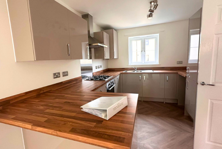 A kitchen with taupe cabinets, a wooden countertop, and a gas hob.