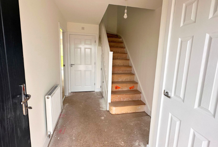 A hallway with a black front door, a radiator, a staircase, and white doors.