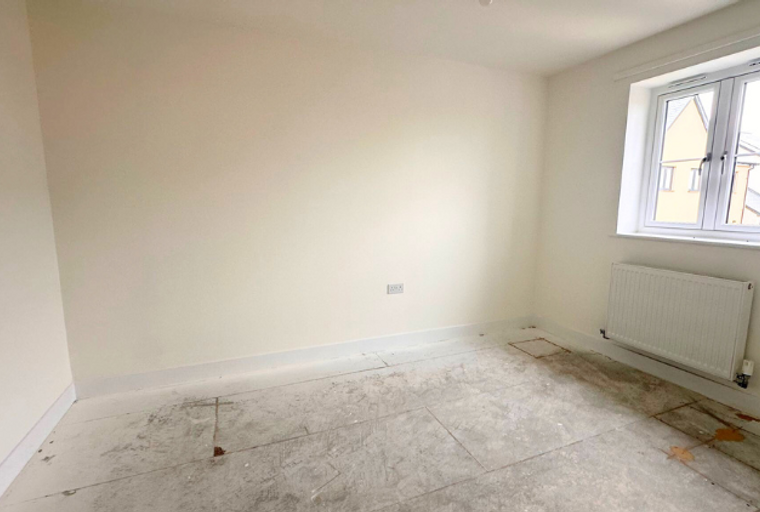 A room with a window, radiator, and unfinished floor.