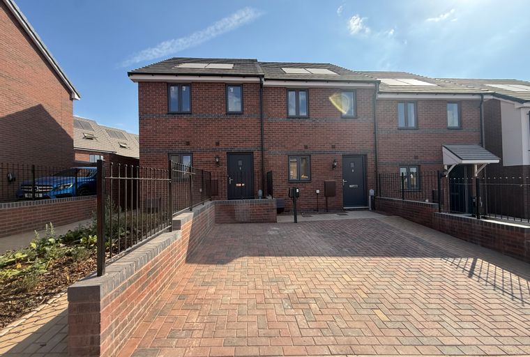 A row of modern brick townhouses with driveways and fences under a blue sky.