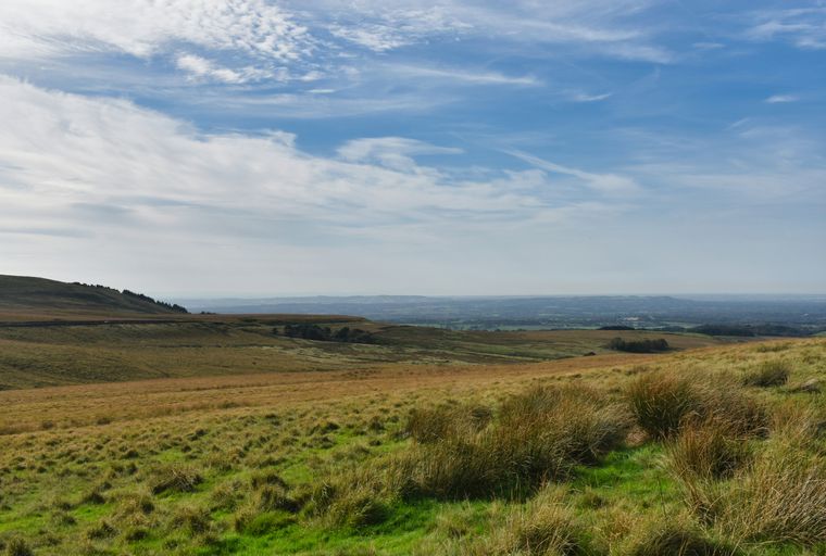 A vast landscape of rolling hills covered in grass under a partly cloudy sky.