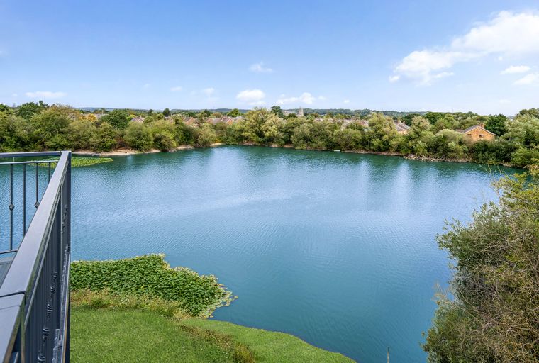 A view of a large blue lake surrounded by trees and houses, with a balcony railing in the foreground.