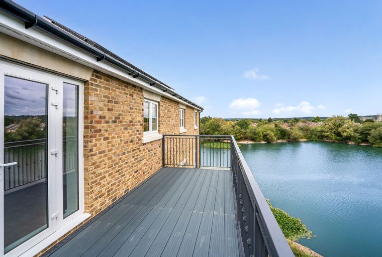 A balcony overlooking a lake with a brick building on the left.