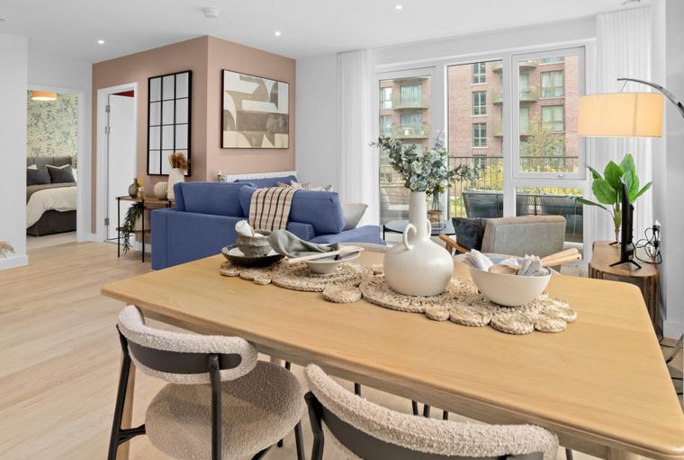 A dining table with chairs in a living room with a sofa and a balcony view.
