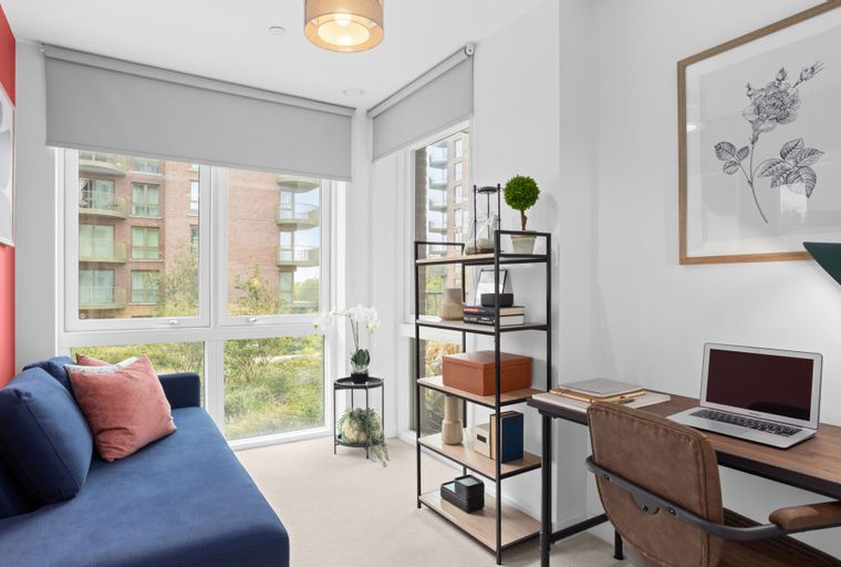 A home office with a blue sofa, a desk with a laptop, and a shelving unit.