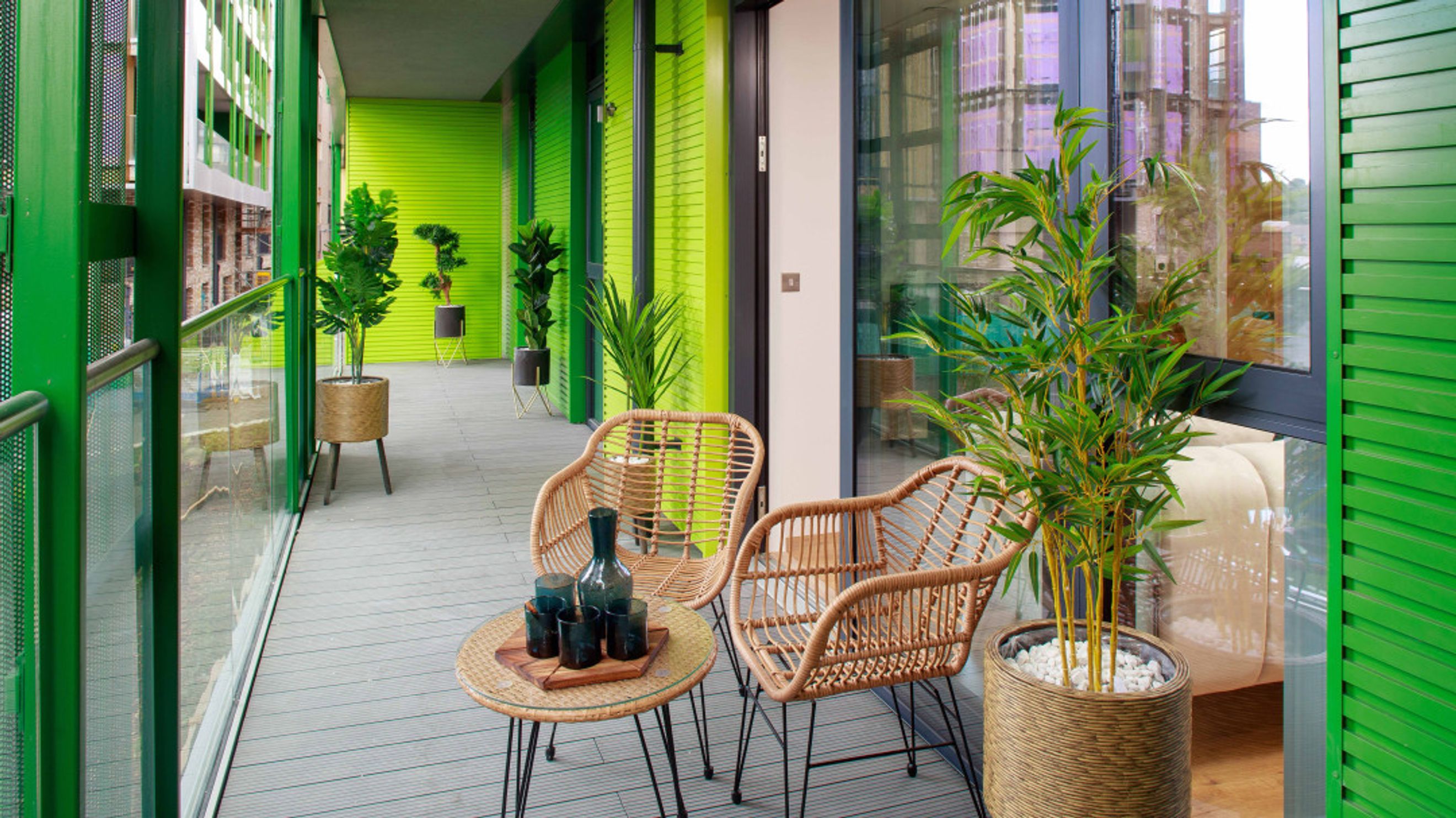 A balcony with two rattan chairs, a small table, and a bamboo plant.