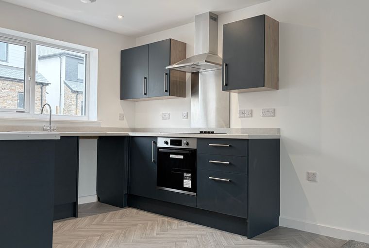 A modern kitchen with dark grey cabinets, a built-in oven, and a window.