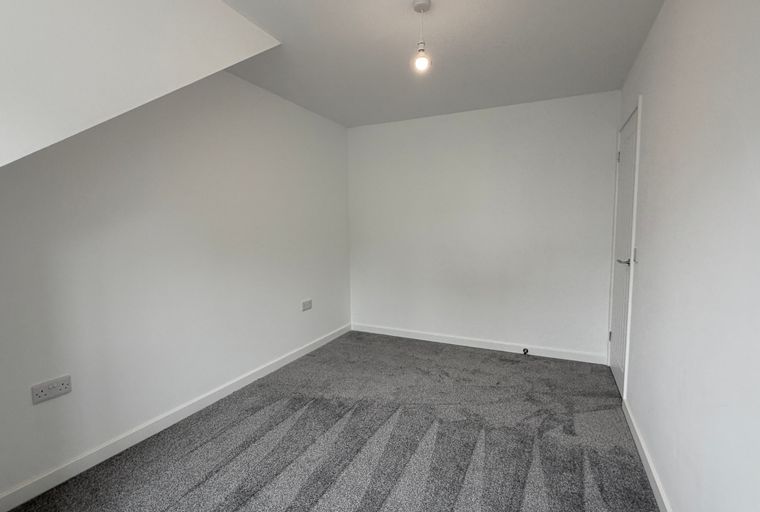 A room with white walls, grey carpet, a pendant light, and power outlets.