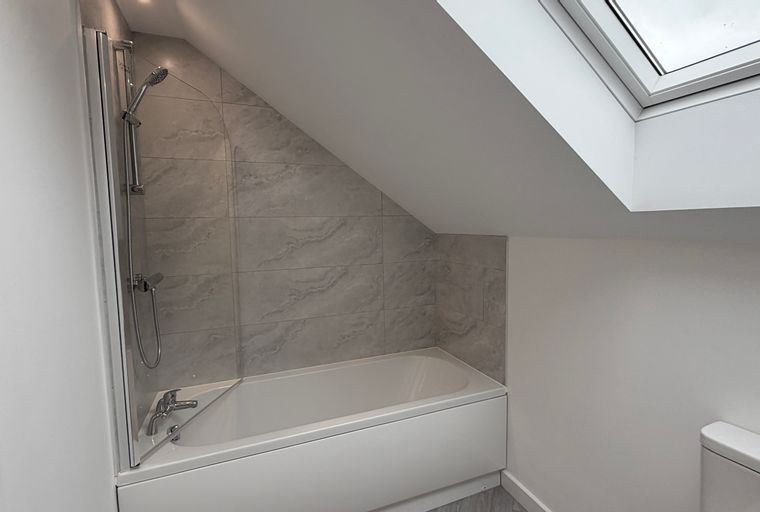 A bathroom with a bathtub, shower, and skylight.