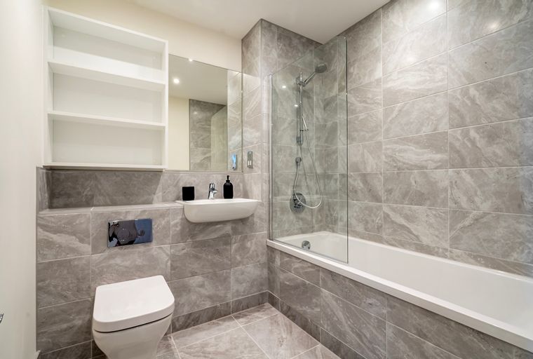 A modern bathroom with a toilet, sink, bathtub with a shower, and shelves.