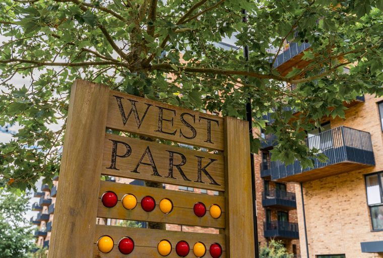A wooden sign that says 'WEST PARK' is in front of a modern apartment building with balconies and trees.