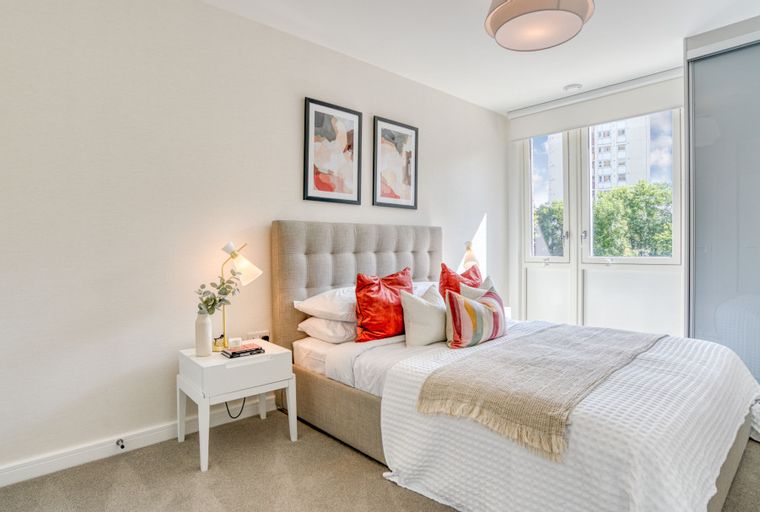 A bedroom with a bed, pillows, a bedside table, and a window.