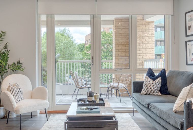 A living room with a sofa, chairs, and a coffee table in front of large glass doors leading to a balcony.
