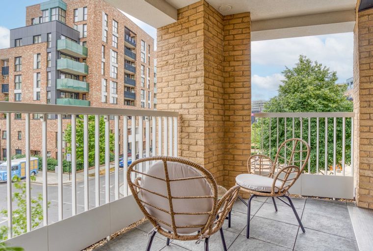 A balcony with two chairs and a view of buildings and trees.