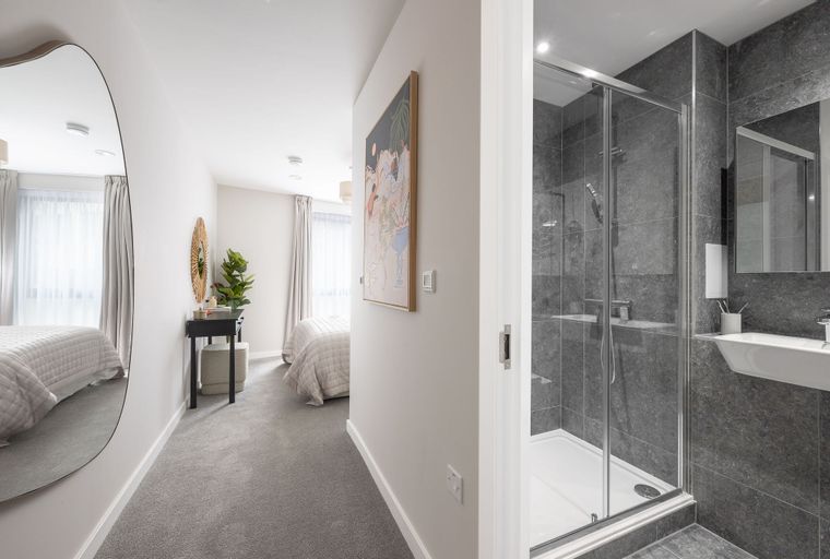 A hallway with a mirror and artwork leading to a bedroom, with a bathroom visible on the side.