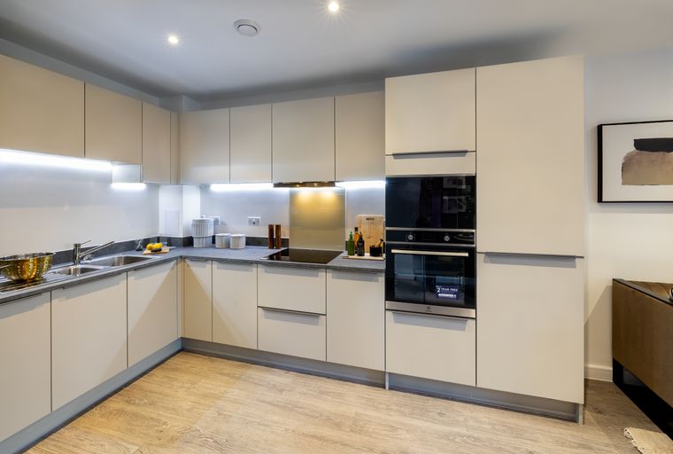 A modern kitchen with light-colored cabinets, a double sink, and integrated ovens.