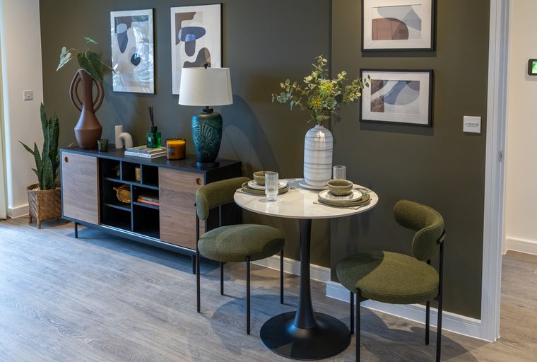 A dining area with a round table, two chairs, and a sideboard.