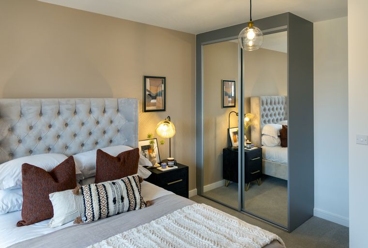 A bedroom with a bed, bedside tables, and a mirrored wardrobe.