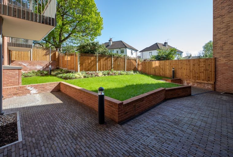 A paved courtyard with a lawn and a wooden fence.