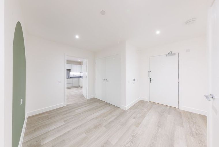 A hallway with a green accent wall, light wood flooring, and multiple doors.