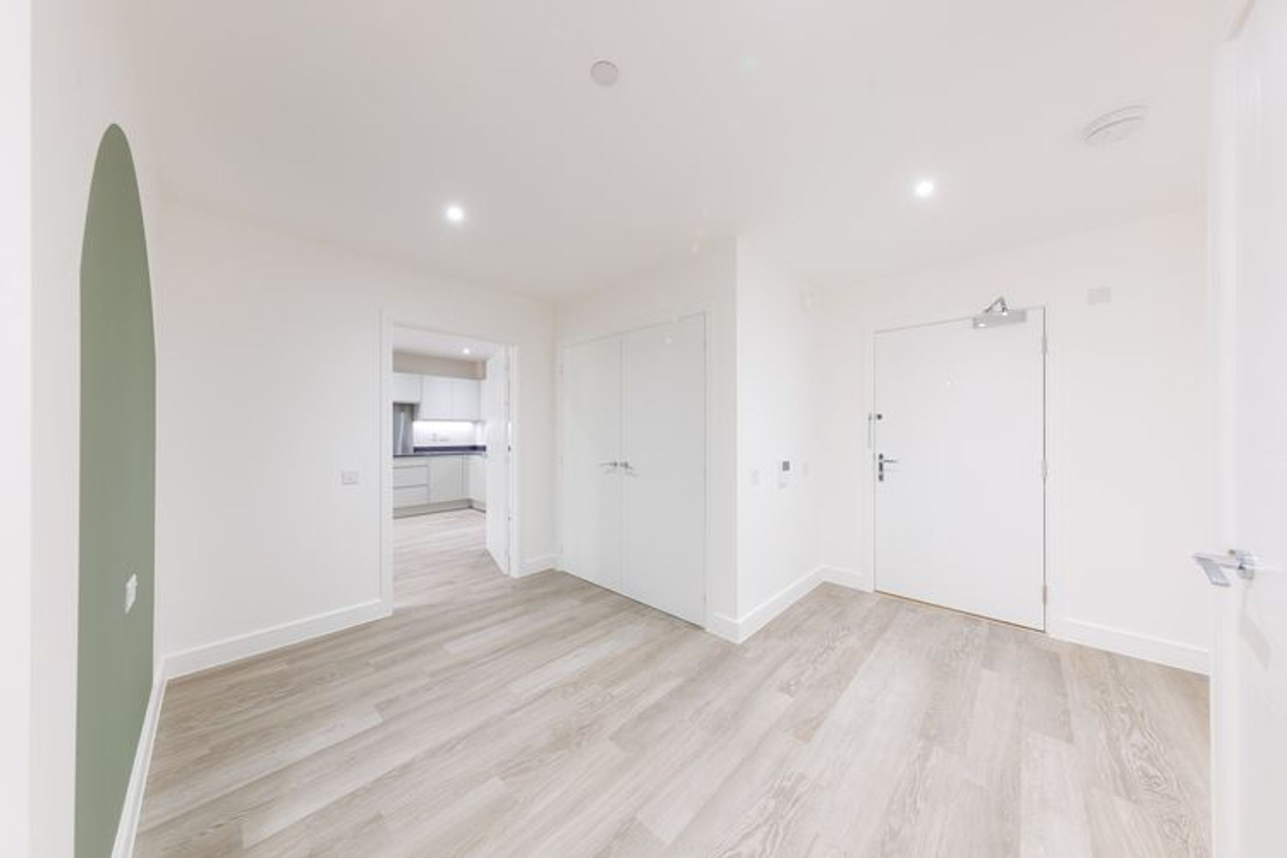 A hallway with a green accent wall, light wood flooring, and multiple doors.
