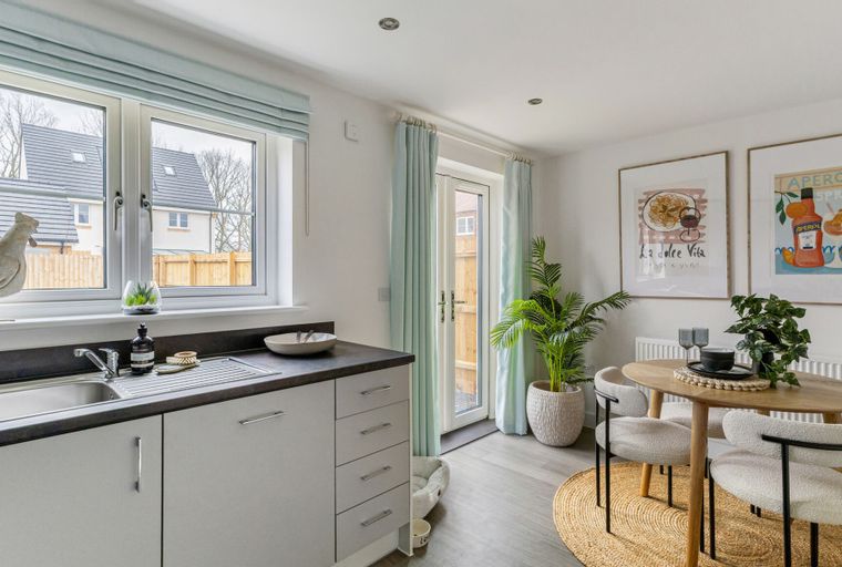A kitchen and dining area with a sink, table, chairs, and artwork on the wall.