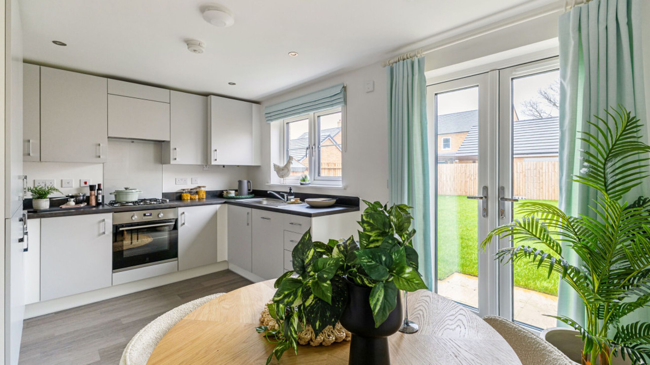 A kitchen with light grey cabinets, a gas stove, a window, and double doors leading to a garden.