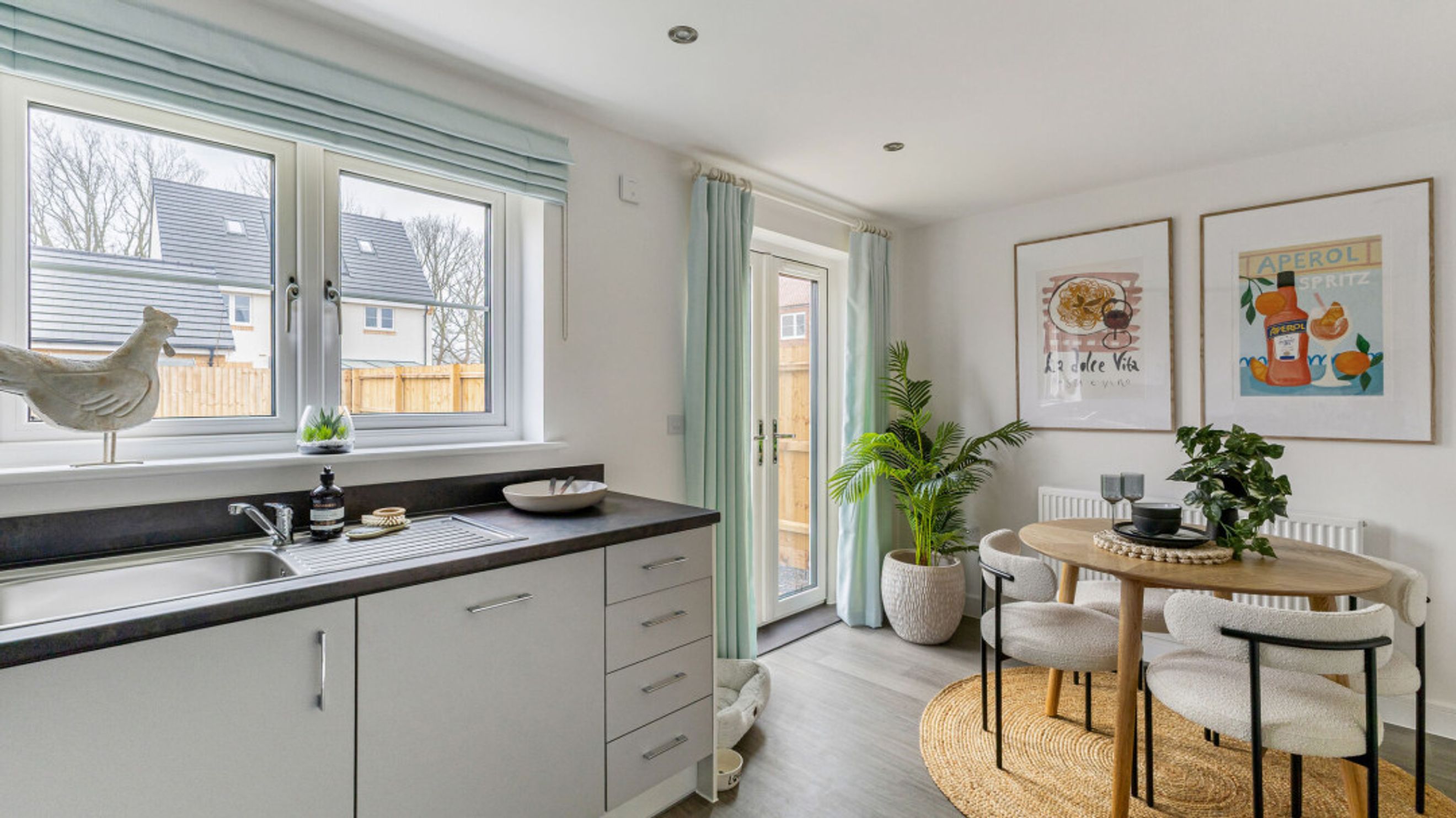 A kitchen and dining area with a sink, table, chairs, and artwork on the wall.