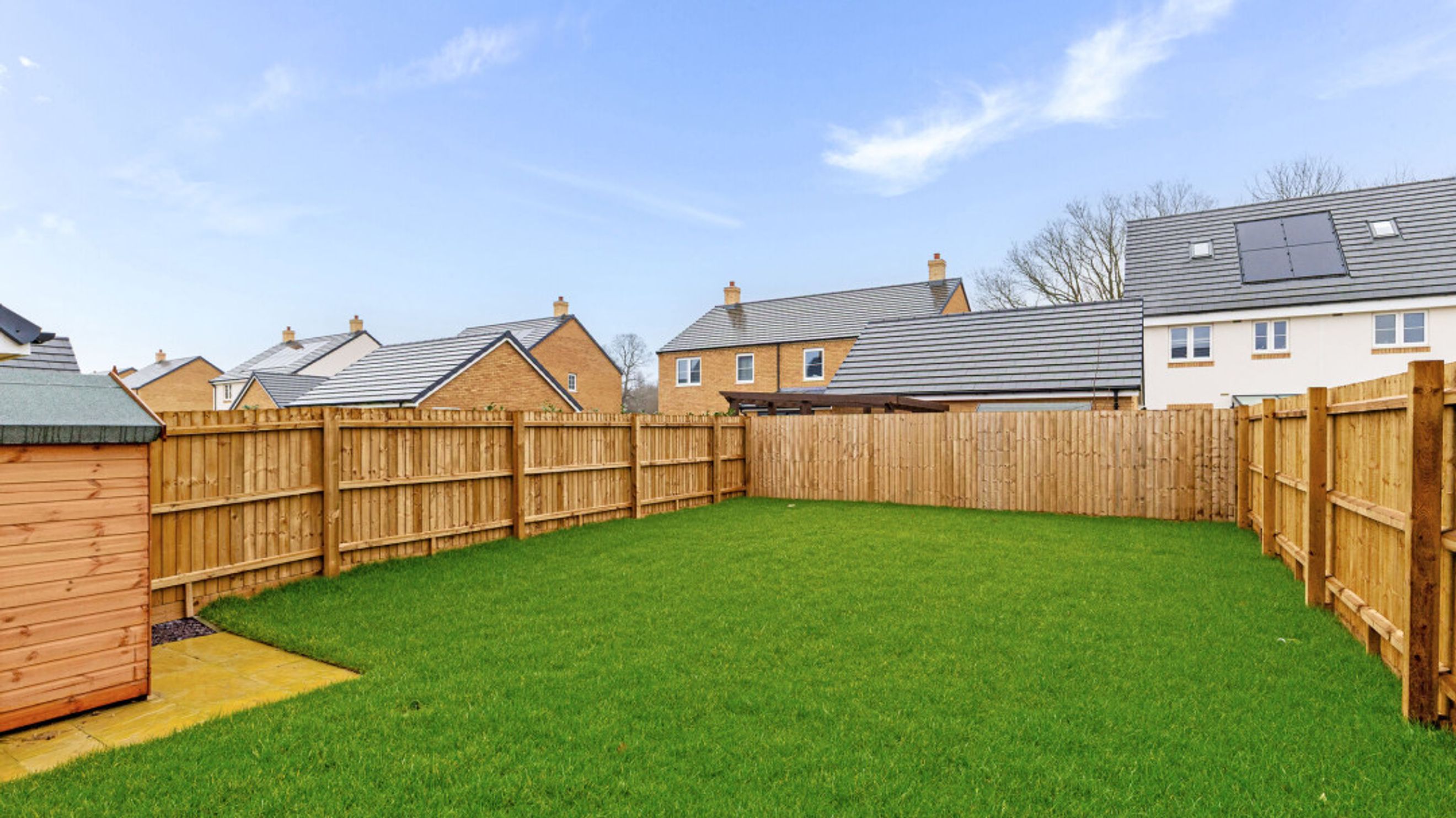 A backyard with a lawn, a wooden fence, and a garden shed.
