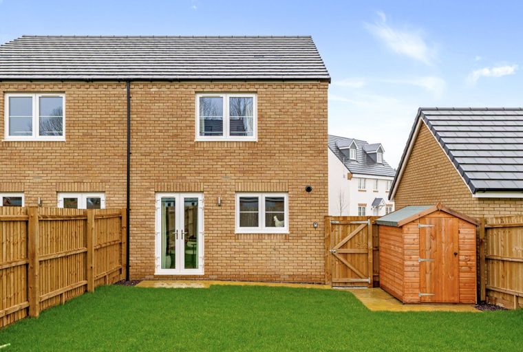 A backyard with a brick house, wooden fence, garden shed, and green lawn.