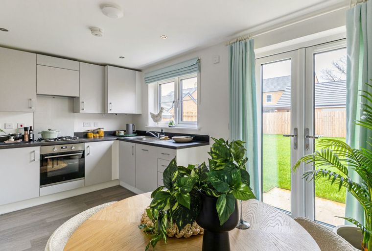 A kitchen with light grey cabinets, a gas stove, a window, and double doors leading to a garden.