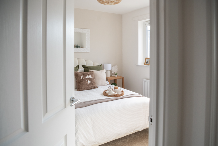 A bedroom with a bed, pillows, a mirror, and a window.